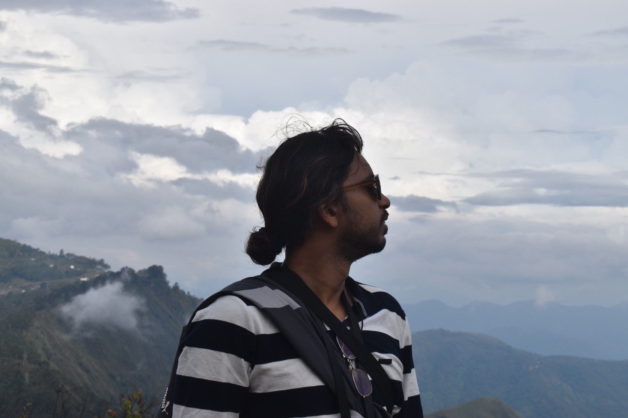 Profile portrait of Aayush against a dramatic mountain skyline and rolling clouds