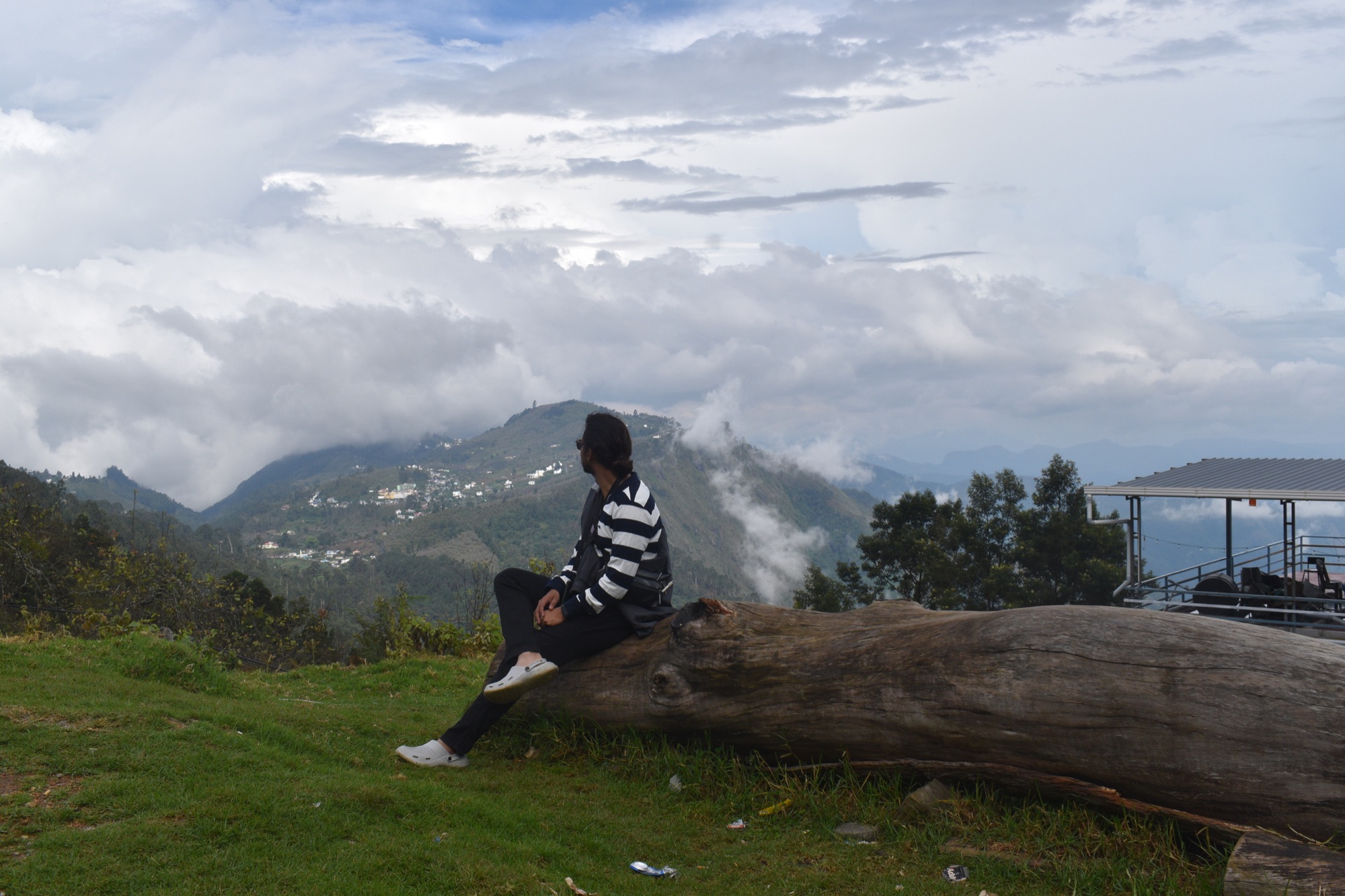 Aayush sitting on a fallen log at a hilltop, overlooking a valley wrapped in low clouds