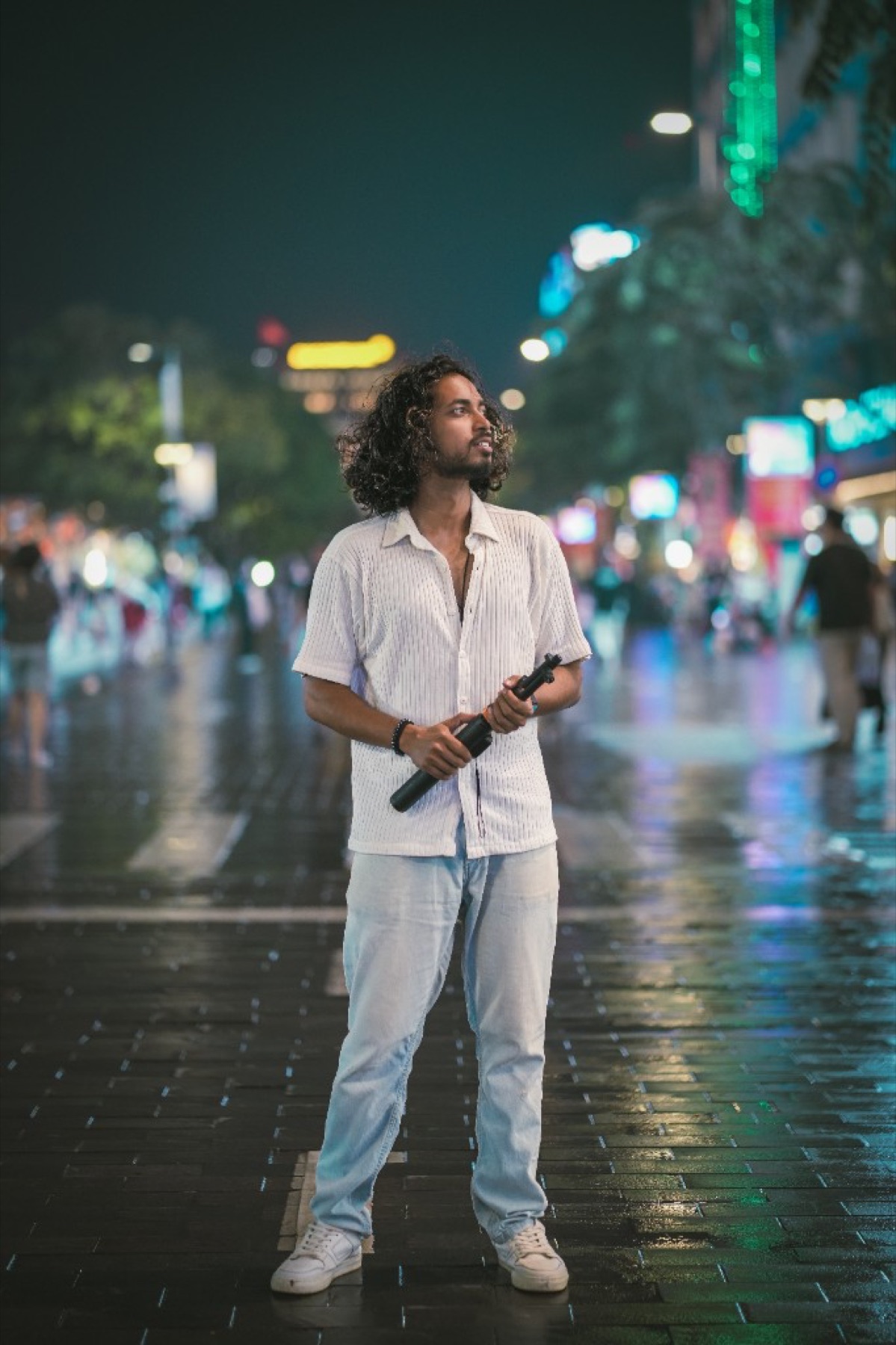 Aayush on a neon-lit, rain-slicked street at night in Vietnam holding a camera grip